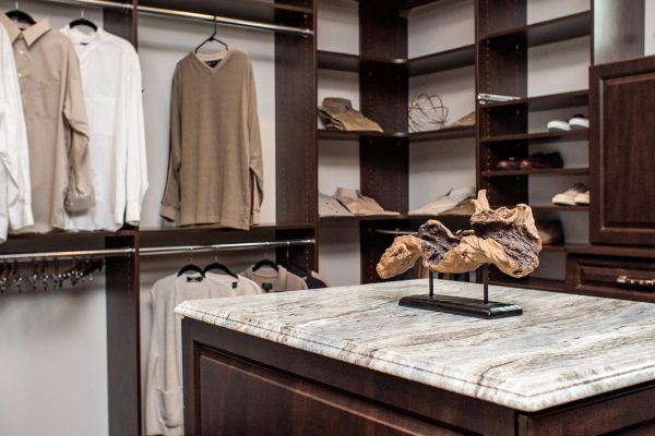 Custom walk-in closet featuring dark wood shelving, hanging clothes, and a marble-topped island with decorative driftwood.