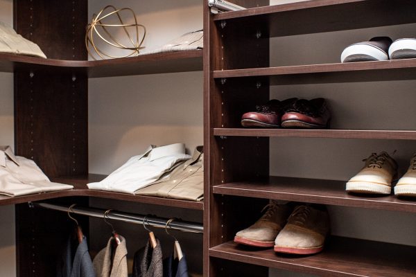 Dark wood custom closet with folded shirts, gold decor, dress shoes, and sneakers on shelves and hanging clothes.