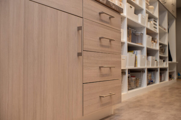 Custom pantry with light wood grain cabinets, silver pulls, and white shelving with clear storage bins.