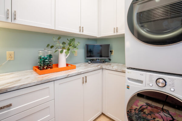 A laundry room with light green walls, white cabinets, marble-like countertops, and stacked LG washer & dryer.