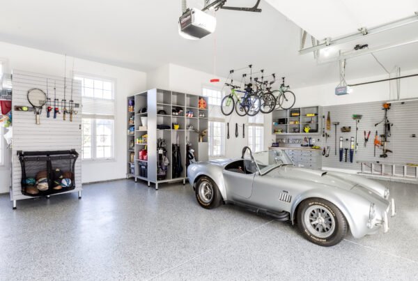A bright and organized two-car garage with a silver gray Shelby Cobra parked on a gray speckled floor.