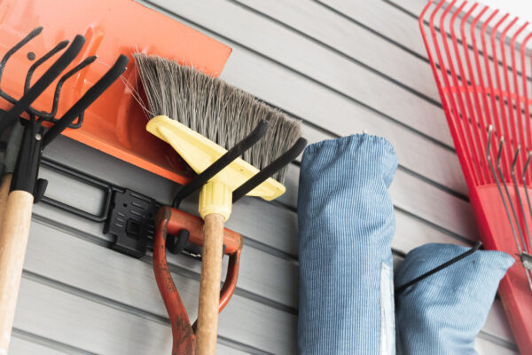 Close-up of garden tools, including a broom, shovel, and rakes, hanging on a slatwall storage system.