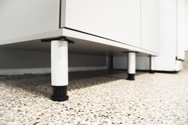 Close-up of white cabinet legs on a speckled, epoxy garage floor.