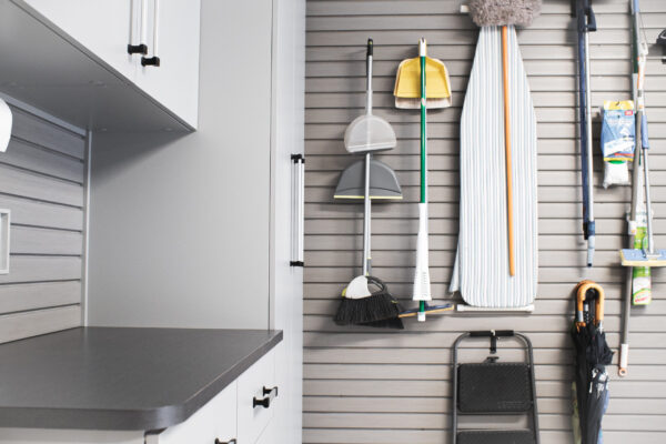 Organized utility storage with a slatwall system holding cleaning supplies, broom, dustpans, and ironing board.