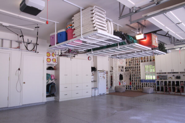 Organized garage with white cabinets and overhead storage racks, hanging bikes, coolers, and various household items.