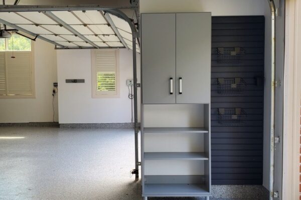 Clean, organized garage with gray epoxy floor, light gray storage cabinet, and dark gray slatwall.