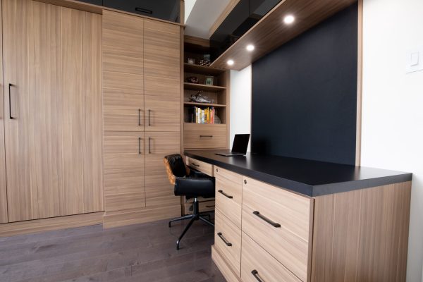 Custom built-in desk and storage unit in a contemporary home office with light wood veneer cabinetry and dark countertops.