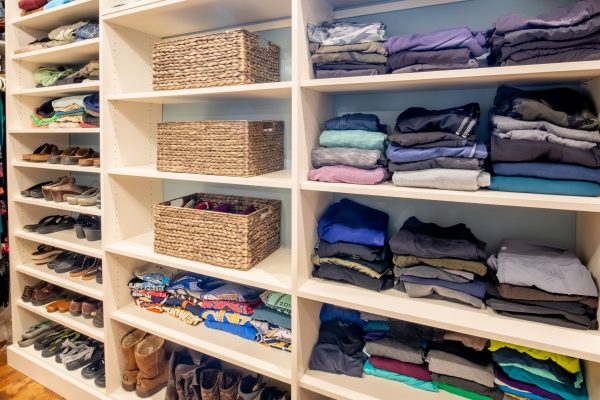 A custom closet with white shelves holding shoes, folded clothes, and woven baskets.
