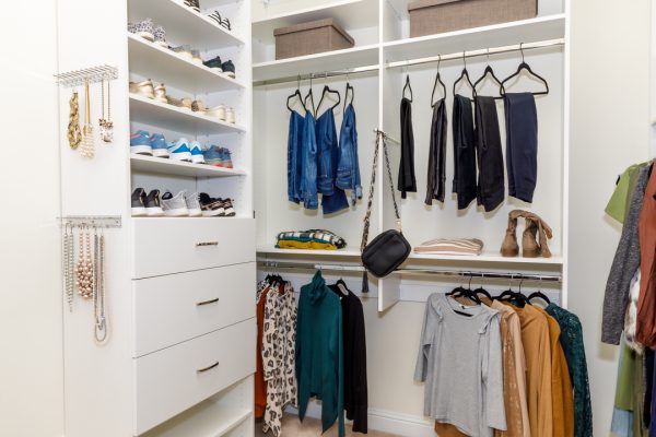 A white walk-in closet with shelves of shoes, hanging clothes, jewelry, and drawers.