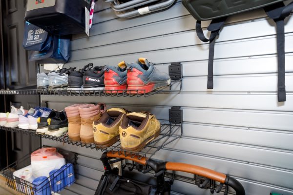 Garage wall organizer with shelves holding various shoes and bags.