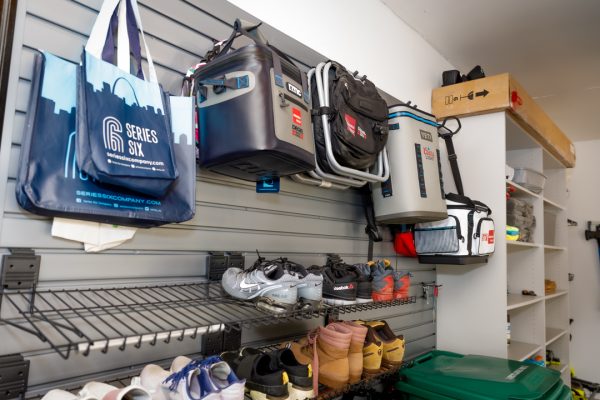 Garage storage system with slatwall, hanging bags, coolers, backpacks, and shoes on wire shelves.