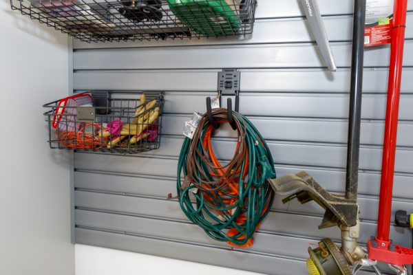 Garage slat wall with storage baskets, coiled extension cords, and gardening tools hanging.