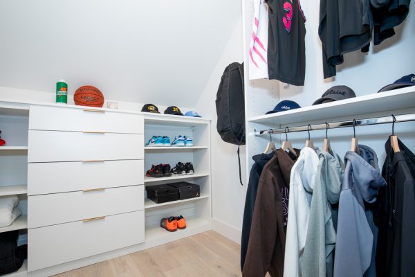 A teen’s white custom closet with drawers, open shelves for sneakers, and racks of clothes.