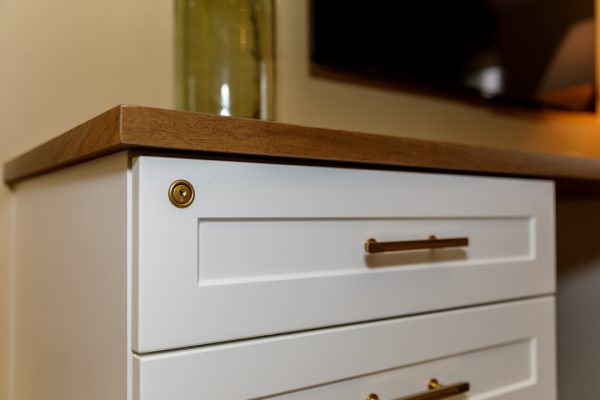 Close-up of modern white cabinet drawers with gold pulls, a brass lock, and a rich wood top.