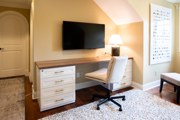 Home office with light yellow walls, a light brown desk, a TV, and a white office chair.