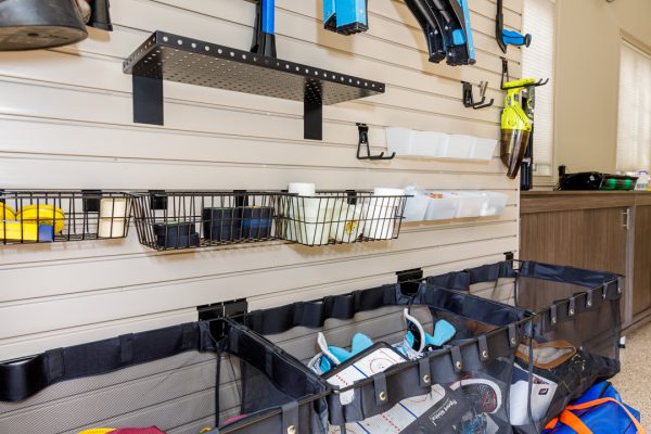 Garage storage with slatwall, black wire baskets, mesh bags, tools, and hockey gear, with a wooden cabinet in the background.