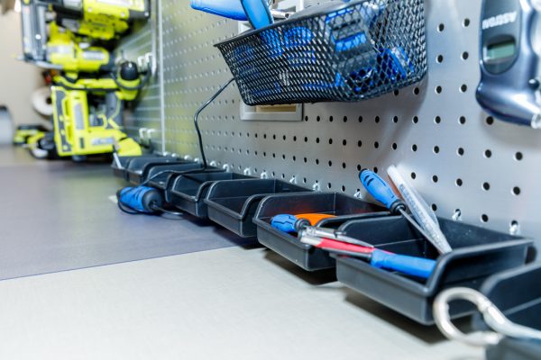 A workshop pegboard with various tools. A metal basket and small bins with screwdrivers and other items hang on the board.