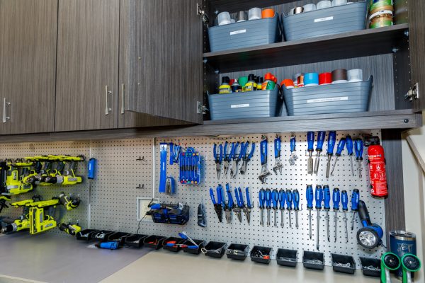 Garage storage with dark wood cabinets, a pegboard wall with power tools and hand tools, and organized gray bins.