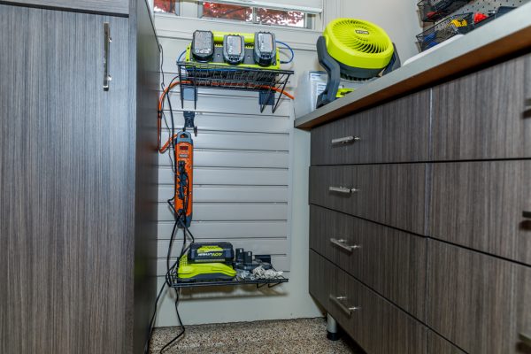 Organized grey garage cabinets with tools and Ryobi batteries charging on a slatted wall panel.