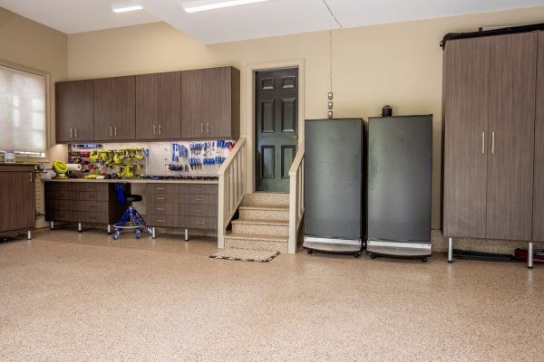 Organized garage with brown cabinets, tool workbench, epoxy floor, and black appliances.