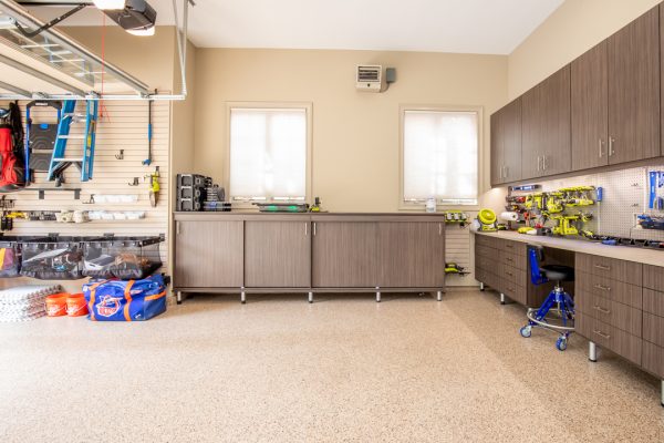 Organized garage with light brown epoxy floor, slatwall storage, dark wood cabinets, workbench, and tools.