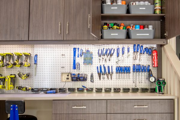 A well-organized garage workbench with gray cabinets, a pegboard displaying tools, and a blue rolling stool.