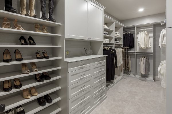 A luxurious, light grey custom walk-in closet with shelves for shoes, hanging racks, and drawers.