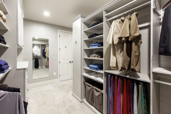 Spacious walk-in closet with light gray shelves, hanging clothes, folded items, full-length mirror, and light carpet.