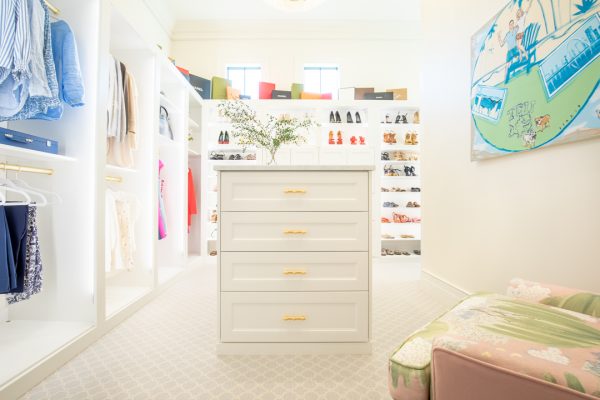 Beautiful white walk-in closet with central dresser, hanging clothes, shoe shelves, and a colorful abstract painting.