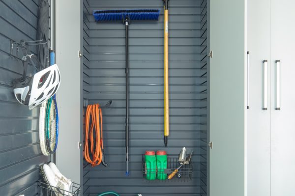 Organized garage with gray slatwall, open cabinet revealing blue broom, yellow rake, green watering can, and red bucket.