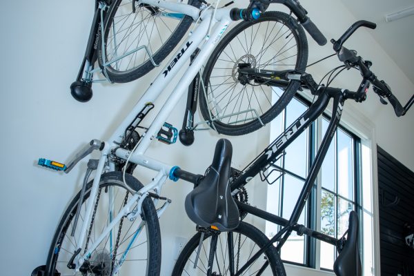 Two bikes are mounted on a white wall. The bikes are a white Trek and a black Trek. There's a window and sports equipment below.