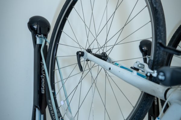 White Trek bicycle hanging vertically on a black Steadyrack bike storage system against a light wall.