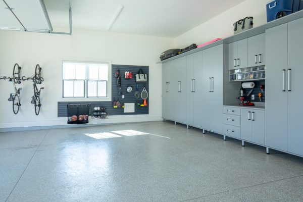 Bright, organized garage with light gray cabinets, gray slatwall storage for sports equipment, and two bicycles on the wall.