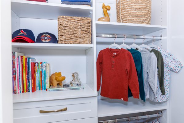 Custom white closet with rows of kid's clothing, hats, books, and woven baskets.