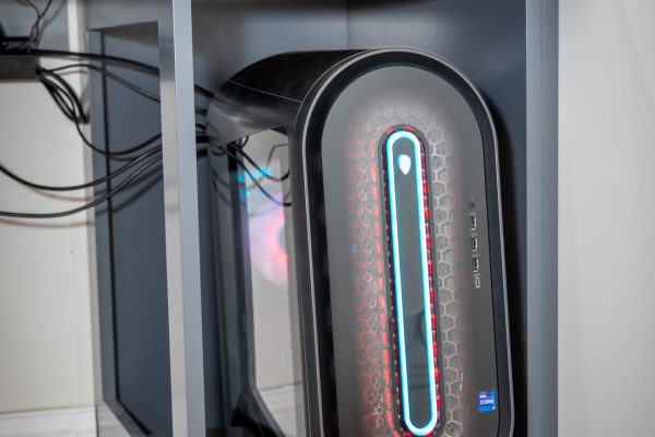 Black Alienware PC tower with blue and red RGB lights, on a pull-out shelf under a wooden desk.